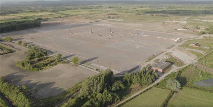 An aerial view of a huge, flat construction site, dotted with piling rigs