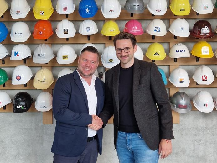 Christoph Miks (director customer solutions, core sensing), Michel Seeger (CEO, Vemaventuri) shake hands in front of a wall of multi-coloured construction hats