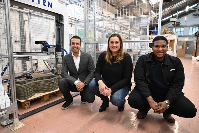 Three people crouch in front of the UK's first 3-D concrete printer