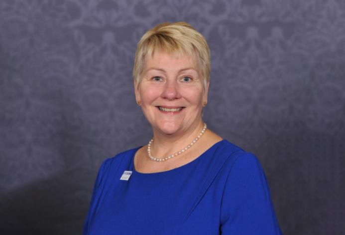 A head and shoulders photo of Caroline Gumble, CEO, Chartered Institute of Building (CIOB), wearing a blue dress, brooch and necklace.