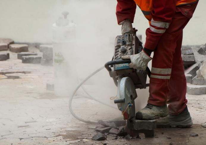 A man in red PPE using a hand-held concrete saw to repair a pavement