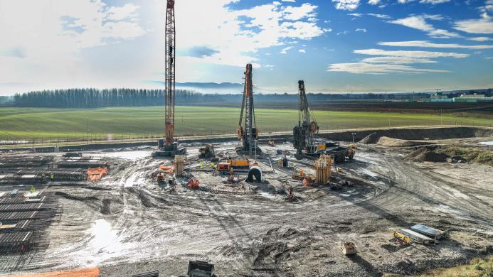 A large open area of country side with a crane and two piling rigs during construction of a circular tank that will be used to store radioactive waste in Slovenia.