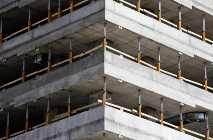 This image depicts a close-up view of a concrete multi-story building under construction, highlighting the raw structural elements such as concrete slabs and metal supports. The image conveys a sense of industrial progress and urban development in a modern city.