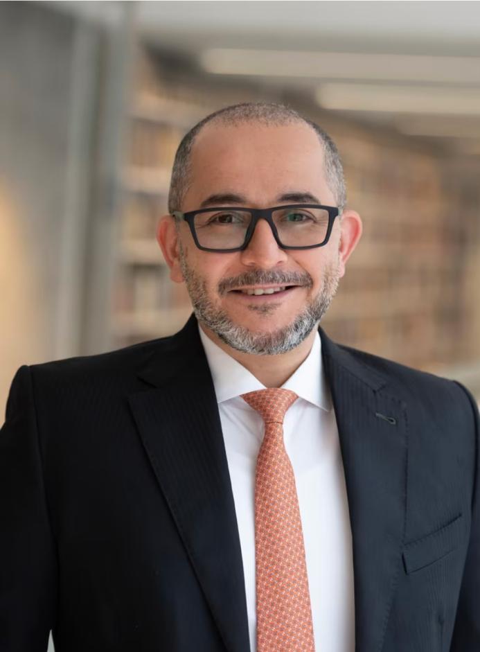 Mohamad Al-Dah, the new IStructE President 2025, in a dark suit, white shirt, glasses and an orange tie.