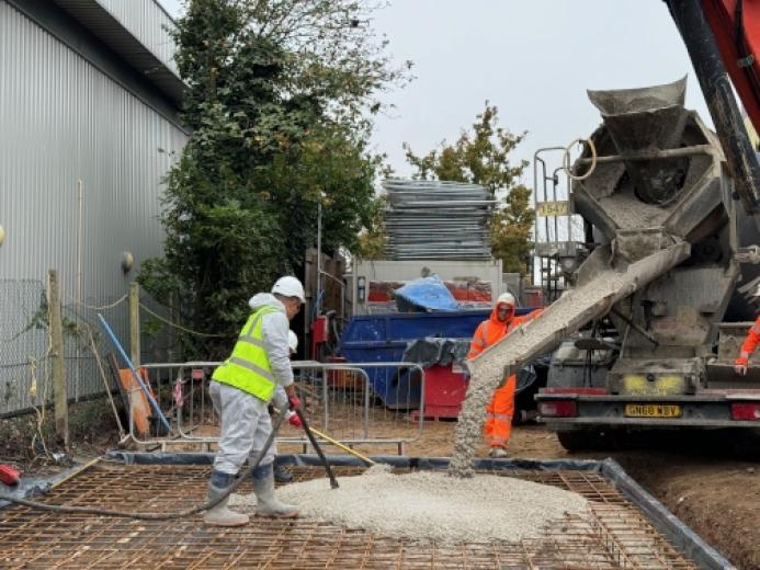 Workers at a construction site spread concrete being discharged by a mobile concrete mixer