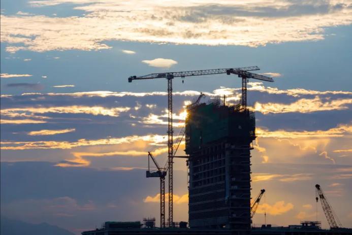 A High rise building under construction in silhouette with the sun setting behind it with three tower cranes