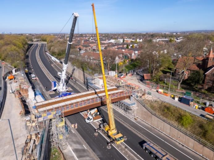 An aerial view of the new M67 St Annes Bridge under construction with a yellow crane on the near side of the bridge and a white crane on the far side.