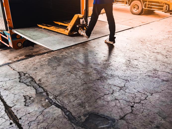 A man using a yellow trolly to unload a lorry onto a loading dock