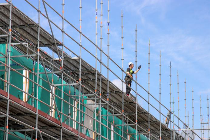A construction worker in hard hat and PPE working on a scaffold.