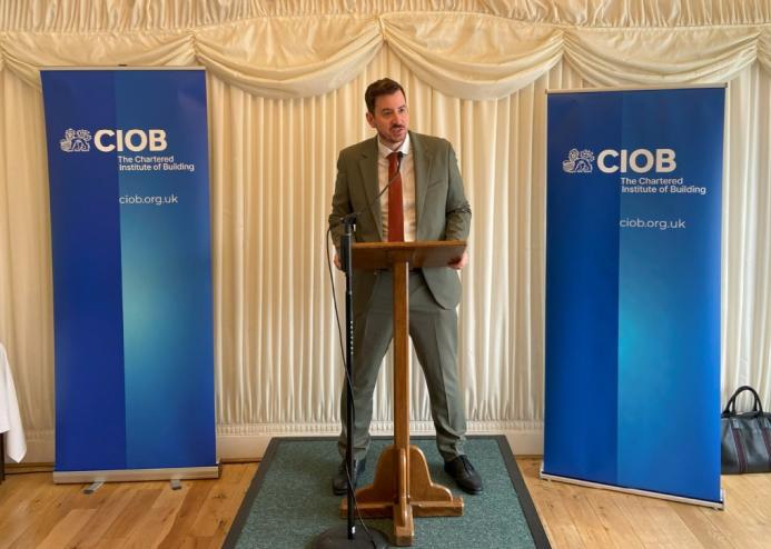 Mike Reader MP, the new chair of the All-Party Parliamentary Group for Excellence in the Built Environment, stands behind a podium, flanked by CIOB banners, speaking at the launch of the CIOB's Construction Client Guide: Leading Projects in the Built Environment, in Parliament last week.