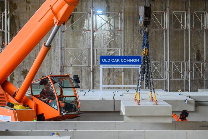 An orange crane and orange PPE-clad worker installing the first platforms at HS2's Old Oak Common station for HS2 trains.
