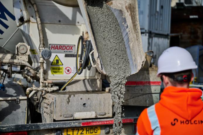 A man in orange PPE and a white hard hat watches low-carbon concrete being delivered for Holcim UK