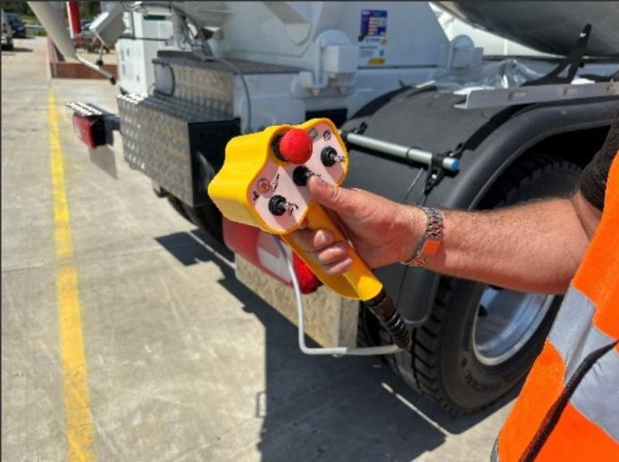 A man in orange PPE holds a yellow concrete drum mixer remote control unit