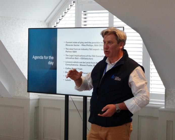 Mike Phillips, CEO British Aggregates Association, wearing a black, fleece gillet, open-necked white shirt and brown chinos, stands in front of a screen, speaking at the BAAs recent Landfill Tax consultation conference.