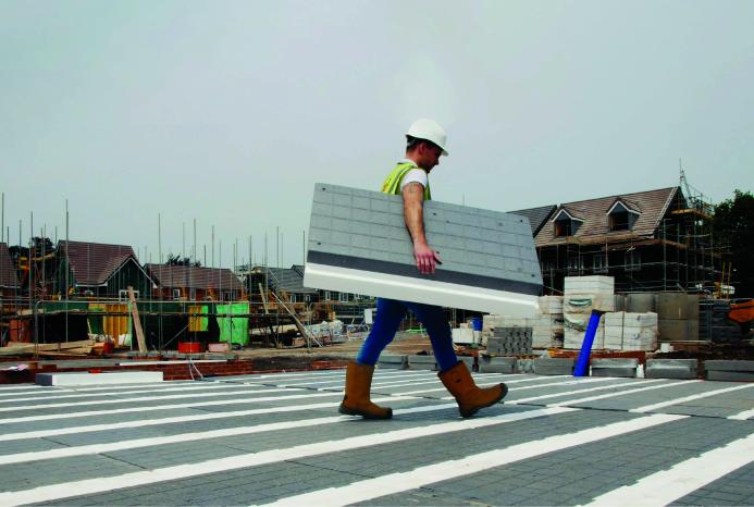 A man in PPE walks across new floor made from Milbank Concrete Products' GDeck, while carrying a panel of the lightweight flooring system.