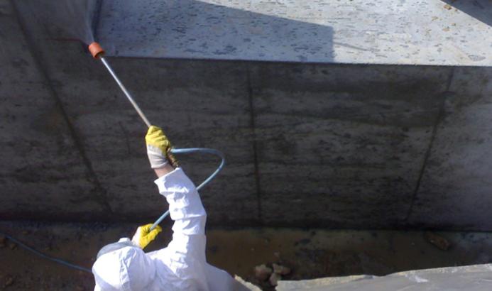 A man in white PPE Waterproofing underground sections of concrete with Vetrofluid using a low pressure pump.