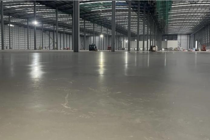A large, newly poured concrete floor inside a large warehouse