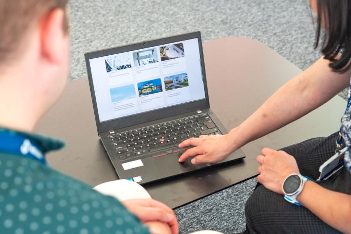 Two people look at a laptop screen which shows several photos and text related to sustainable construction