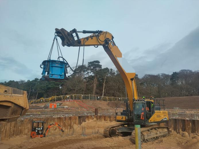 A yellow excavator lifts a blue pile cropper at the Port of Nigg, Scotland