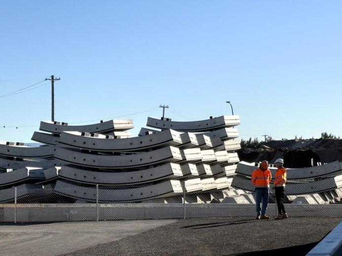 Two men in orange PPE stand next to a stack of precast concrete tunnel segments at the Western Harbour Tunnel Precasting facility in Emu Plains.