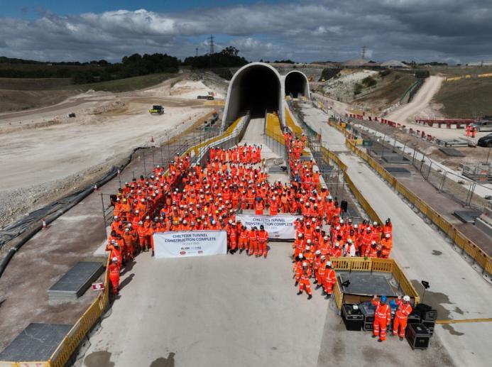A large crowd of constructions workers in orange PPE stand by the entrance to the recently completed Chiltern Tunnel, HS2’s longest, which is now structurally complete following five years of construction. 