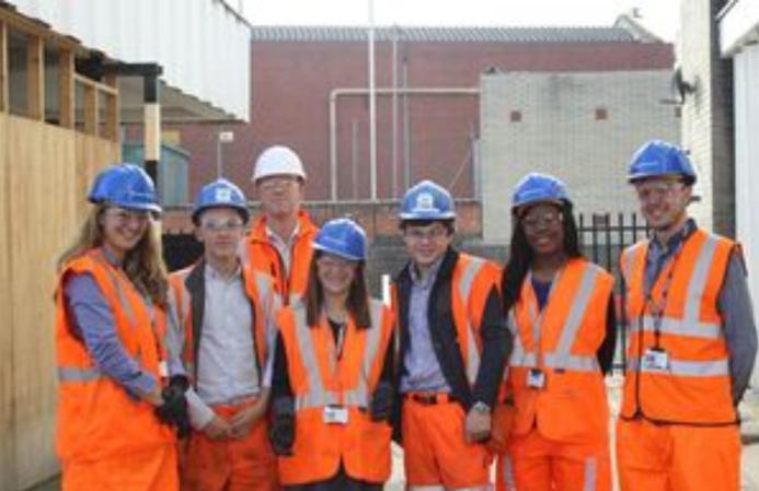 A group of students wearing orange PPE and blue hard hats stand outside a college of FE to celebrate the launch of the The new Construction Technical Excellence Colleges, which will train young people and career switchers in core trades including groundworks and bricklaying.