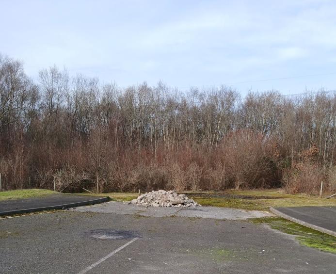 A dead-end road with a pile of illegally dumped concrete hardcore, with trees in the background.