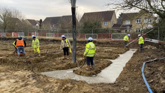 Men in yellow PPE watch as concrete is discharged from a chute for foundations at a new housing development