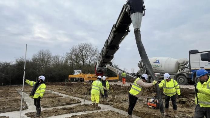 construction workers in yellow PPE lay concrete that's being delivered via chute from a concrete mixer