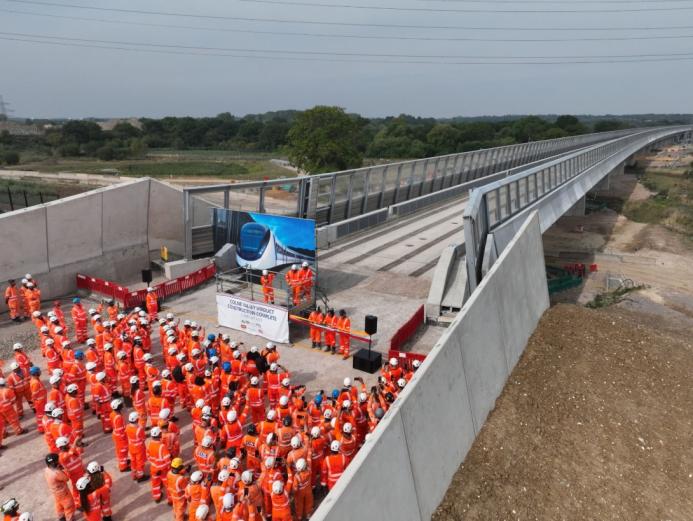 A large group of orange-clad PPE wearing construction workers gather at one end of the colne Valley Viaduct. Over 3,600 m³ of concrete was poured to form the kerb along the 3.4 km Colne Valley Viaduct – now structurally complete.
