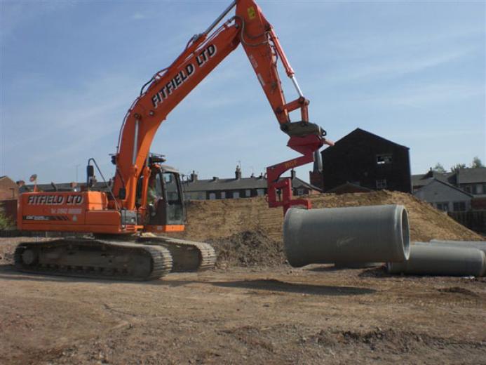 An orange excavator lifts a concrete pipe