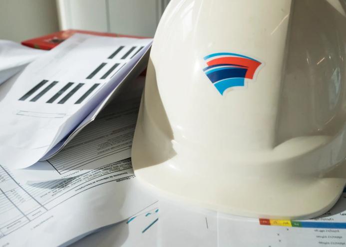 A white hard hat with red and blue insignia, and technical construction papers on a table