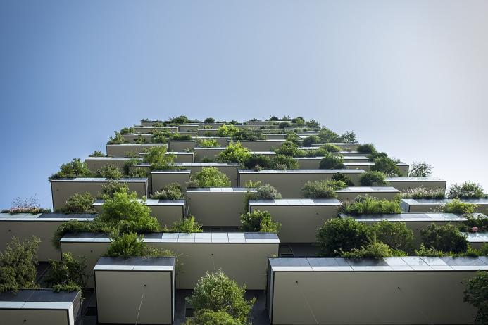 Looking up at the exterior of a high-rise building which features balconies covered in plants