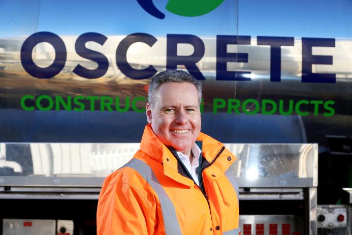 Oscrete director Scott Wilson stand in front of an Oscrete sign wearing orange PPE