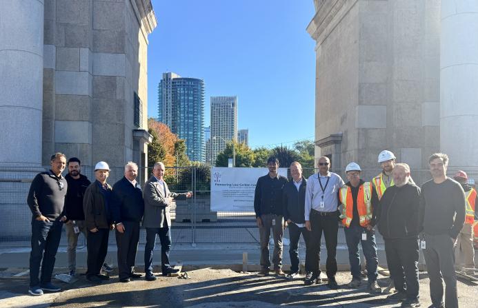 A group of people in business wear and PPE celebrate the use of Bio Graphene Solutions’ graphene-enhanced low-carbon concrete beneath Toronto’s historic Princes’ Gates at Exhibition Place.
