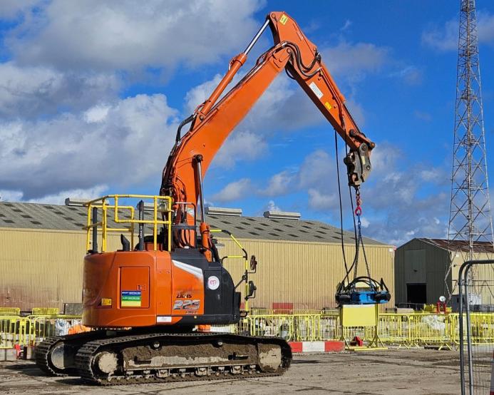 An orange, zero tail-swing midi excavator lifts a pile cropper on a construction site
