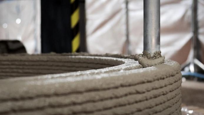 A close-up of a 3D concrete printer nozzle in action
