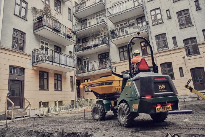 A yellow site dumper being driven in front of an urban construction site