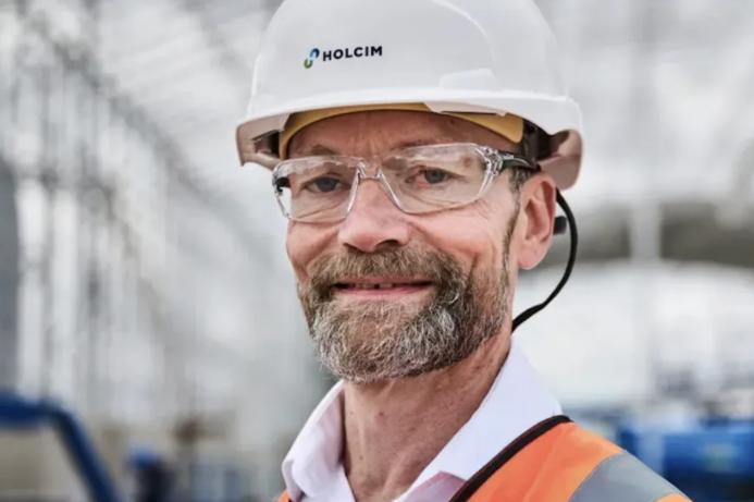 A head and shoulders photo of a man with a beard and glasses wearing PPE and a white hard hat