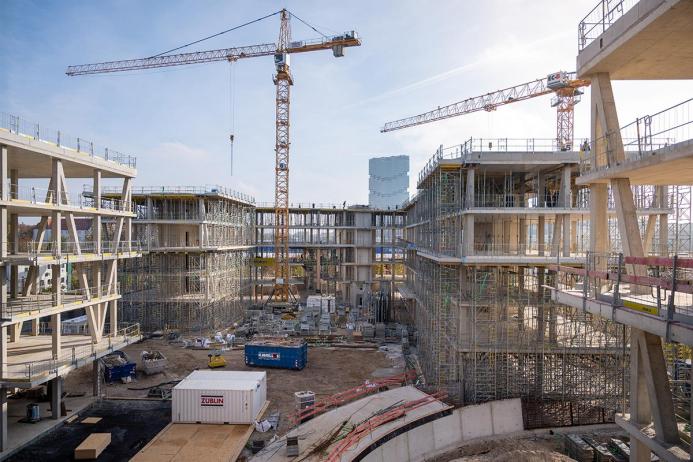 An under construction mid-rise building with two tower cranes in the background