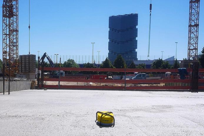 A yellow Doka Concremote sensor embedded in concrete with a high-rise building in the background
