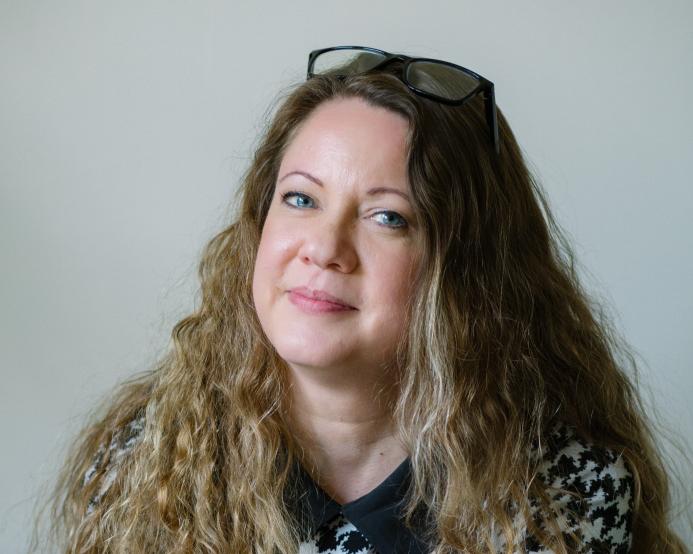 A head shot of Laila Morris, newly appointed practice director at Betts Associates, with long curly hair, a checked top and glasses on her head