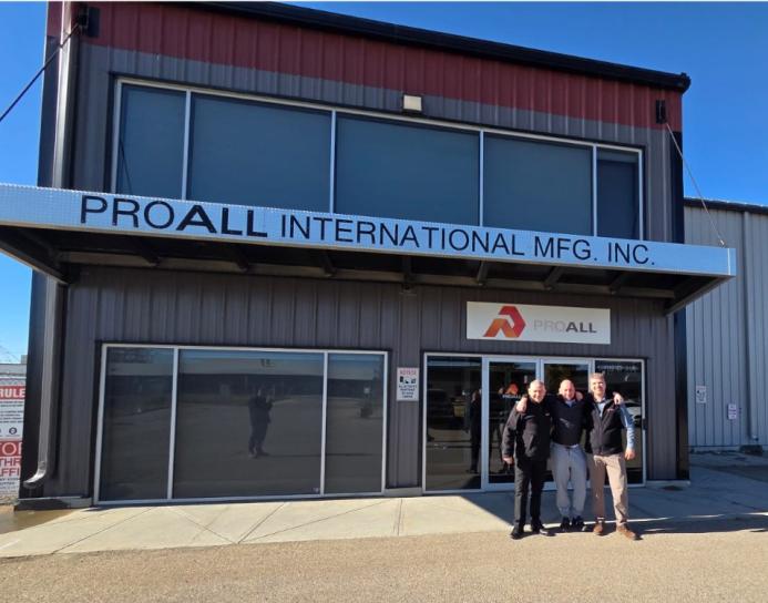Three men stand awith hands on each other's shoulders outside a two storey, ProAll branded building