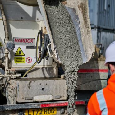 A man in orange PPE and a white hard hat watches low-carbon concrete being delivered for Holcim UK