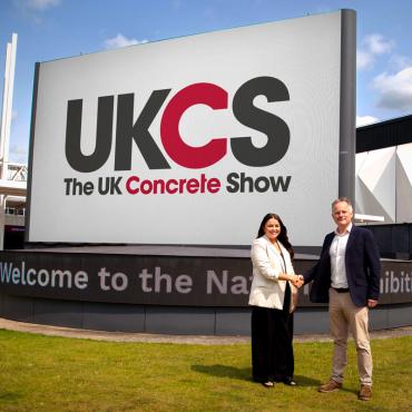 Richard Bradbury (right), Managing Director of The QMJ Group with Helaena Ackers, Exhibition Sales Account Manager, The NEC shake hands outside the NEC in front of a huge UK Concrete Show sign, following the signing of a two-year deal that sees the flagship trade show to stay at Birmingham’s NEC through 2027, with free parking and expanded plans for 2026 edition