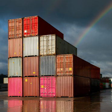 Multi-coloured containers stacked up in a yard with storm clouds and a rainbow in the background