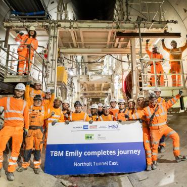 A large group of people in orange PPE, part of HS2 tunnelling team celebrates, TBM Emily completing 5.5km journey. Image: HS2.