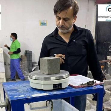 A man with a beard, waring a dark shirt inspects a concrete cube in a testing laboratory.