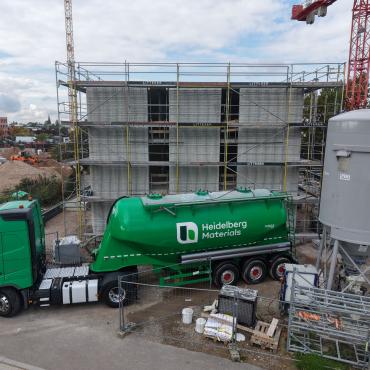 A green, Heidelberg Materials' cement truck in front of an under construction house