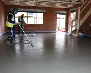 Two men in yellow PPE using screeds to level and internal concrete floor
